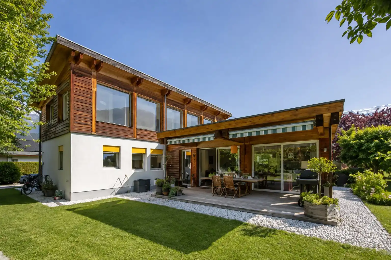 La façade en bois d’une villa et sa terrasse couverte, ouvertes sur la pelouse