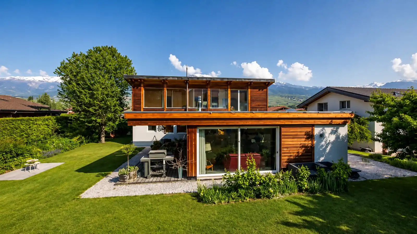 Une villa en bois vue depuis son jardin, la vallée et les sommets enneigés derrière